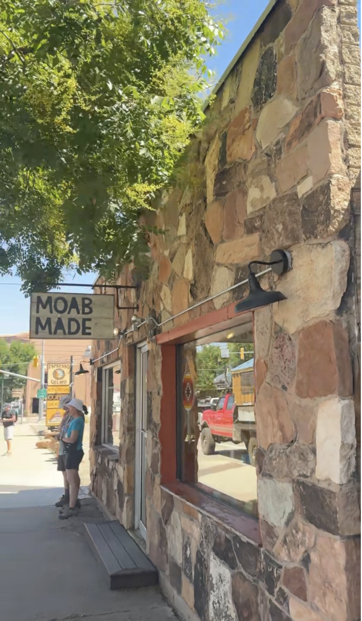 Two people standing outside of a stone and brick building with a wooden sign that reads "Moab Made" in Moab, Utah