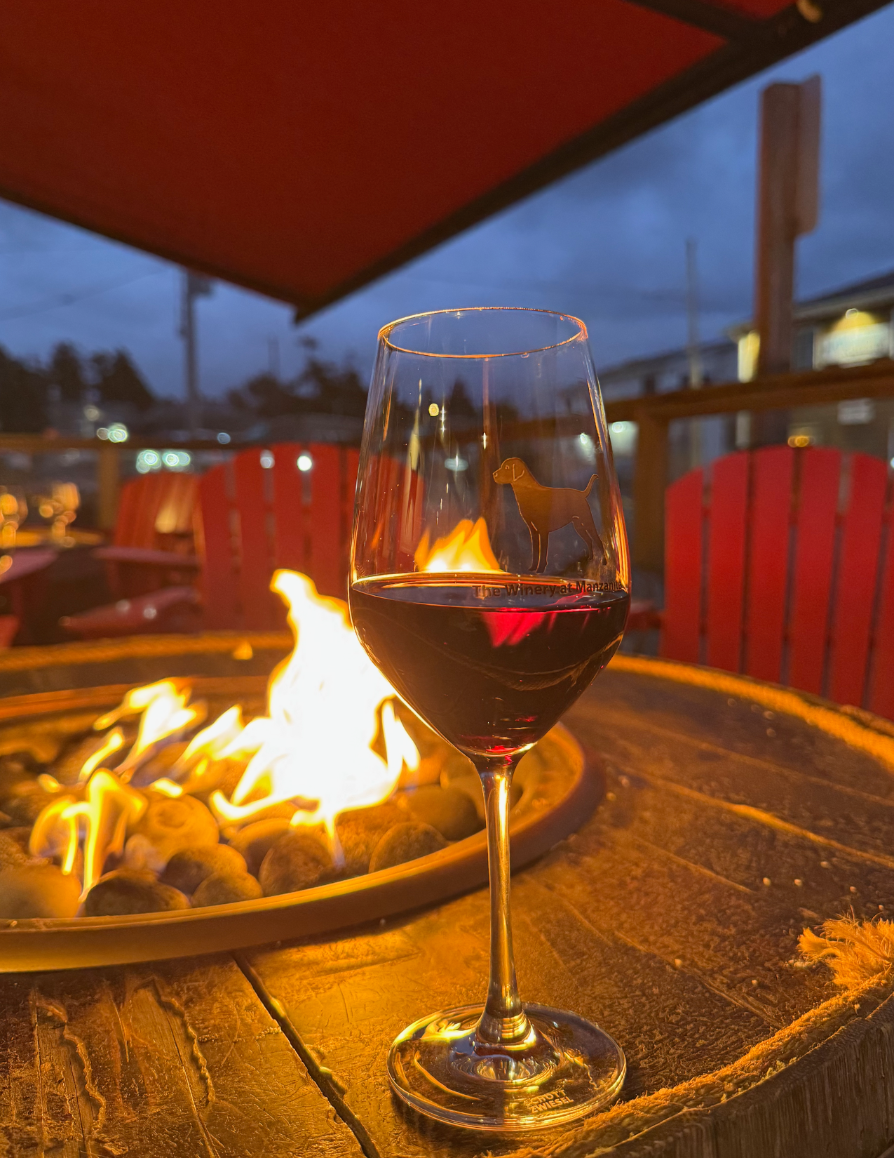 Glass of red wine with a dog picture on the glass on a wooden table with a fire pit at The Winery at Manzanita in Manzanita, Oregon
