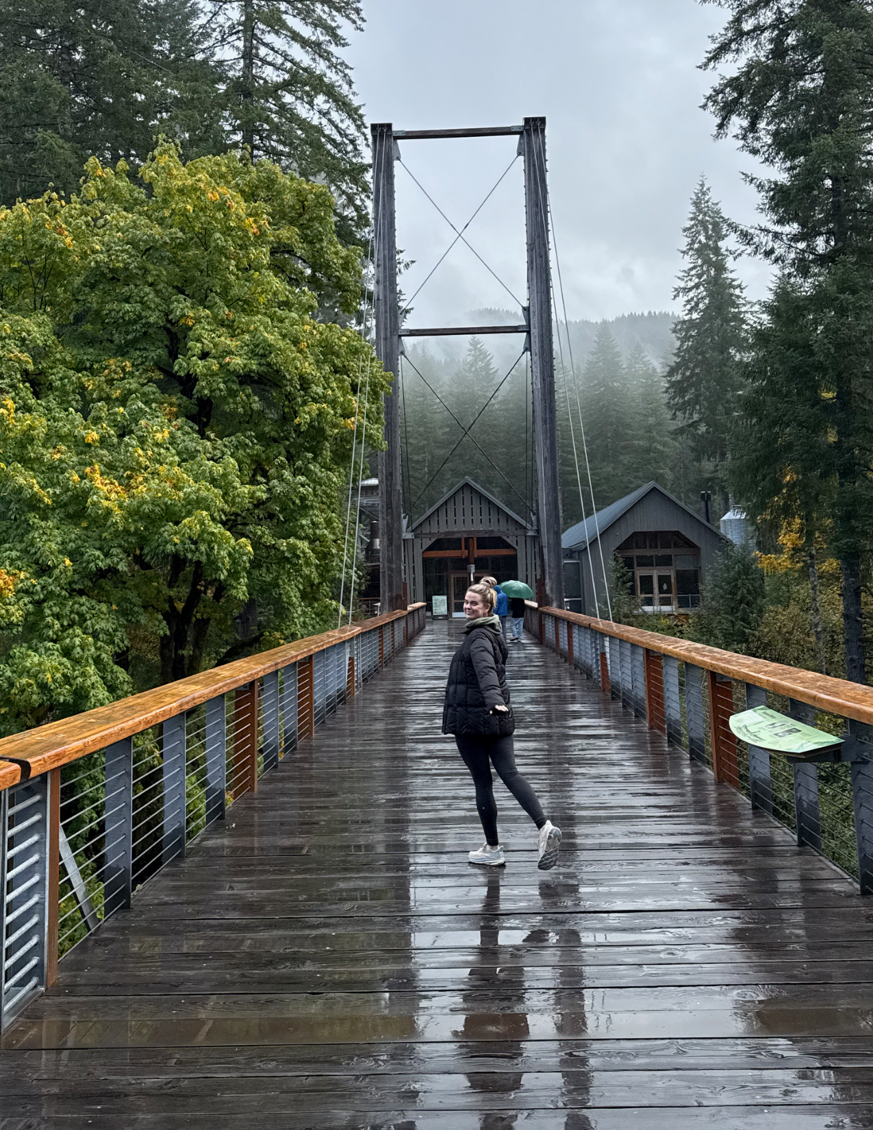 Woman standing on wooden suspension bridge in the rain at Tillamook Forest Center in Tillamook, Oregon