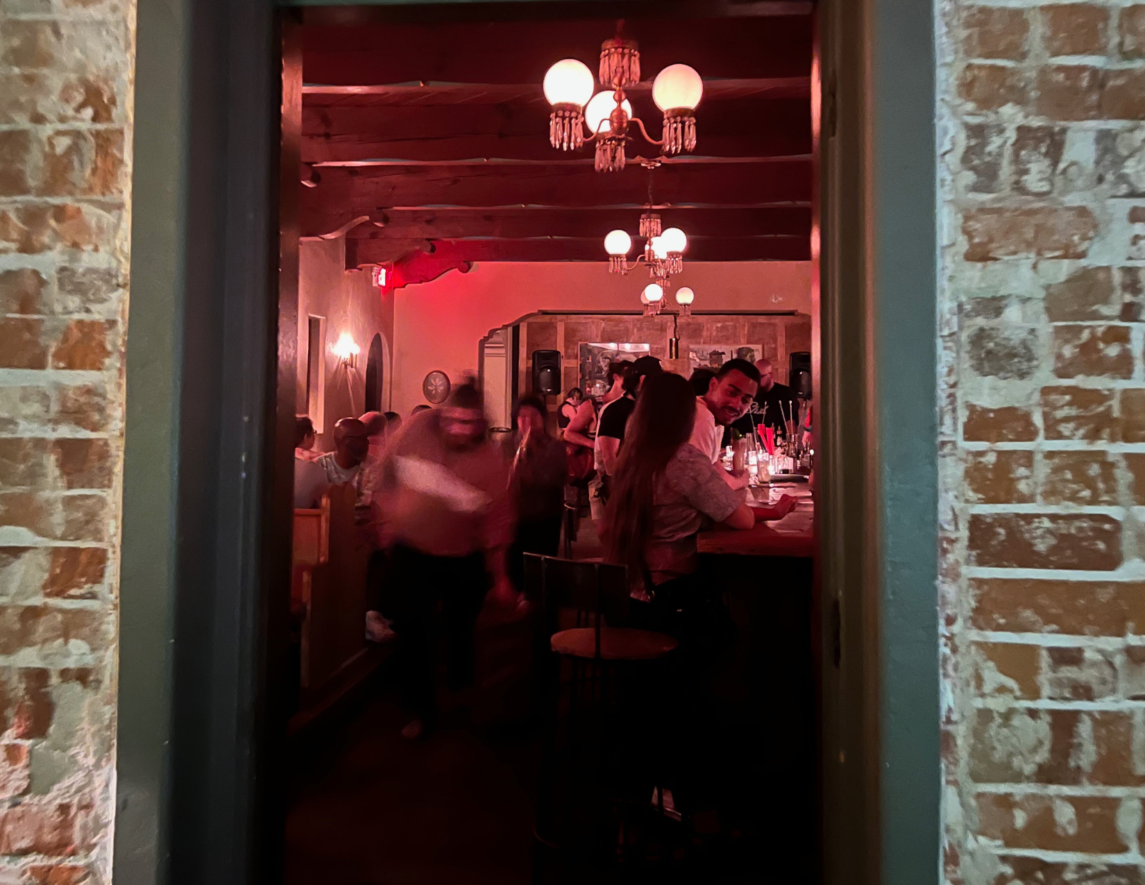 Guests gather inside The Owl's Club, a mortuary-turned-speakeasy featuring vintage lighting, exposed brick, and craft cocktails.