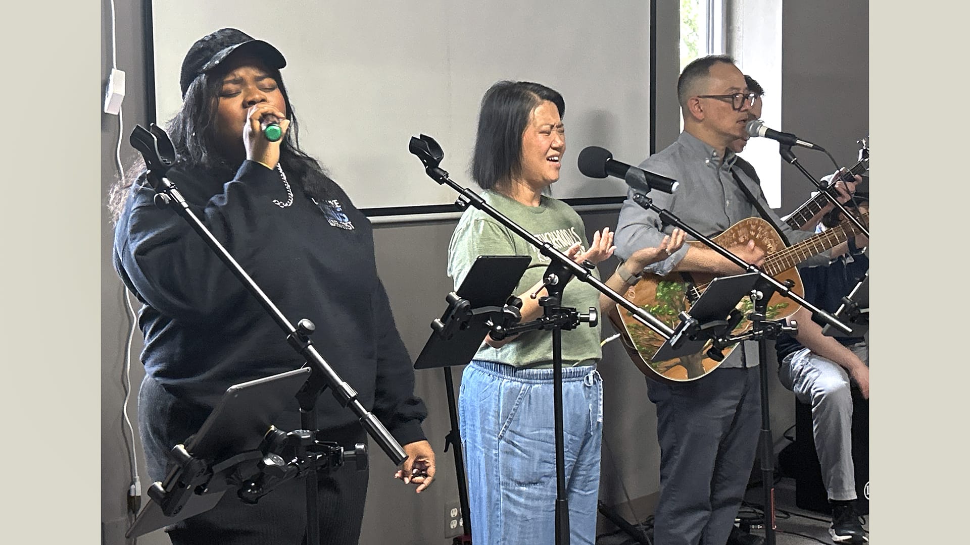 Two women and one man sing at microphones.