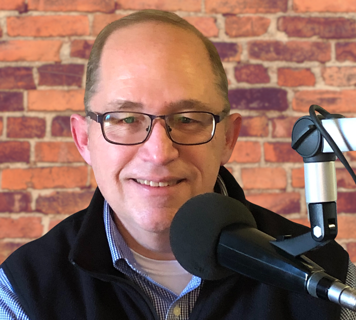 Middle-aged man smiling as he sits in front of a microphone.