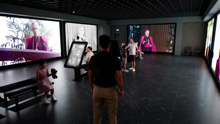 Visitors stand in a dark museum-style gallery watching large video screens showing archival footage of a Catholic bishop.