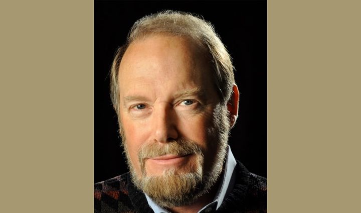 A man with a sandy beard and nice smile looks intently at the camera.