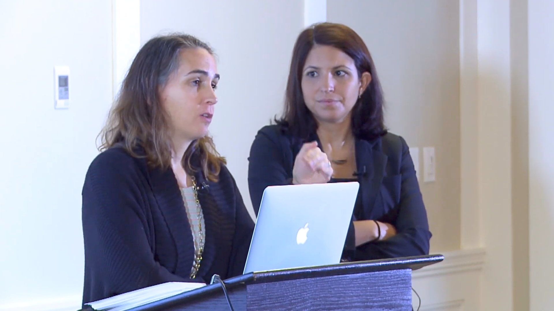 Two neuro-oncology doctors speaking at a podium with a laptop
