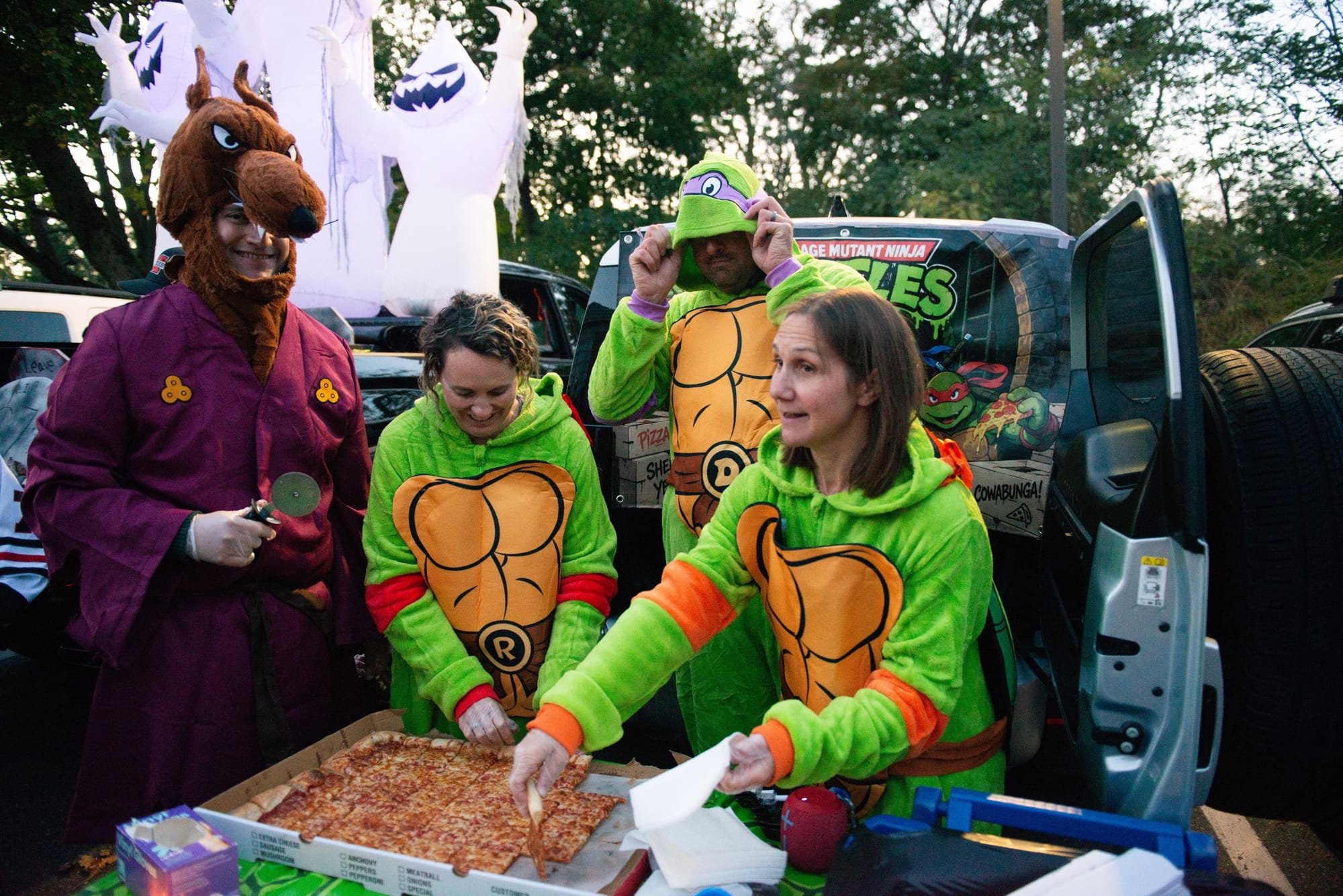 Shawn Hoskins, from left, Patrice Hoskins, David Gainer and Meghan Gainer dress as Master Splinter and Teenage Mutant Ninja Turtles characters as they serve pizza from their trunk at Glover