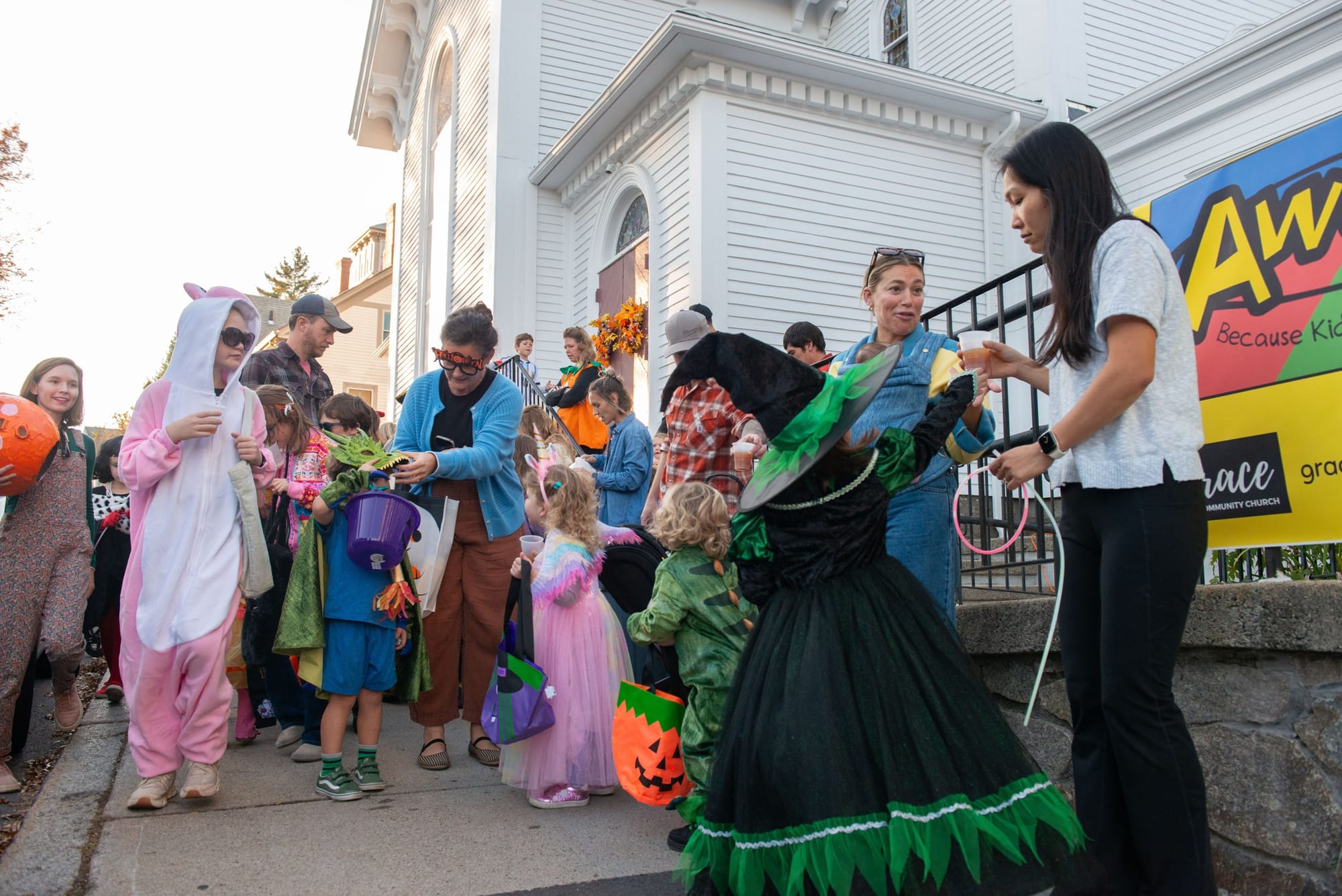 Costumed children line up for treats outside a white church