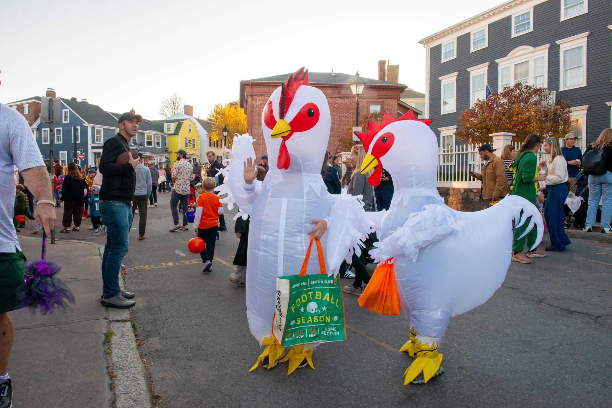 Two people in inflatable white chicken costumes carry candy bags down a street