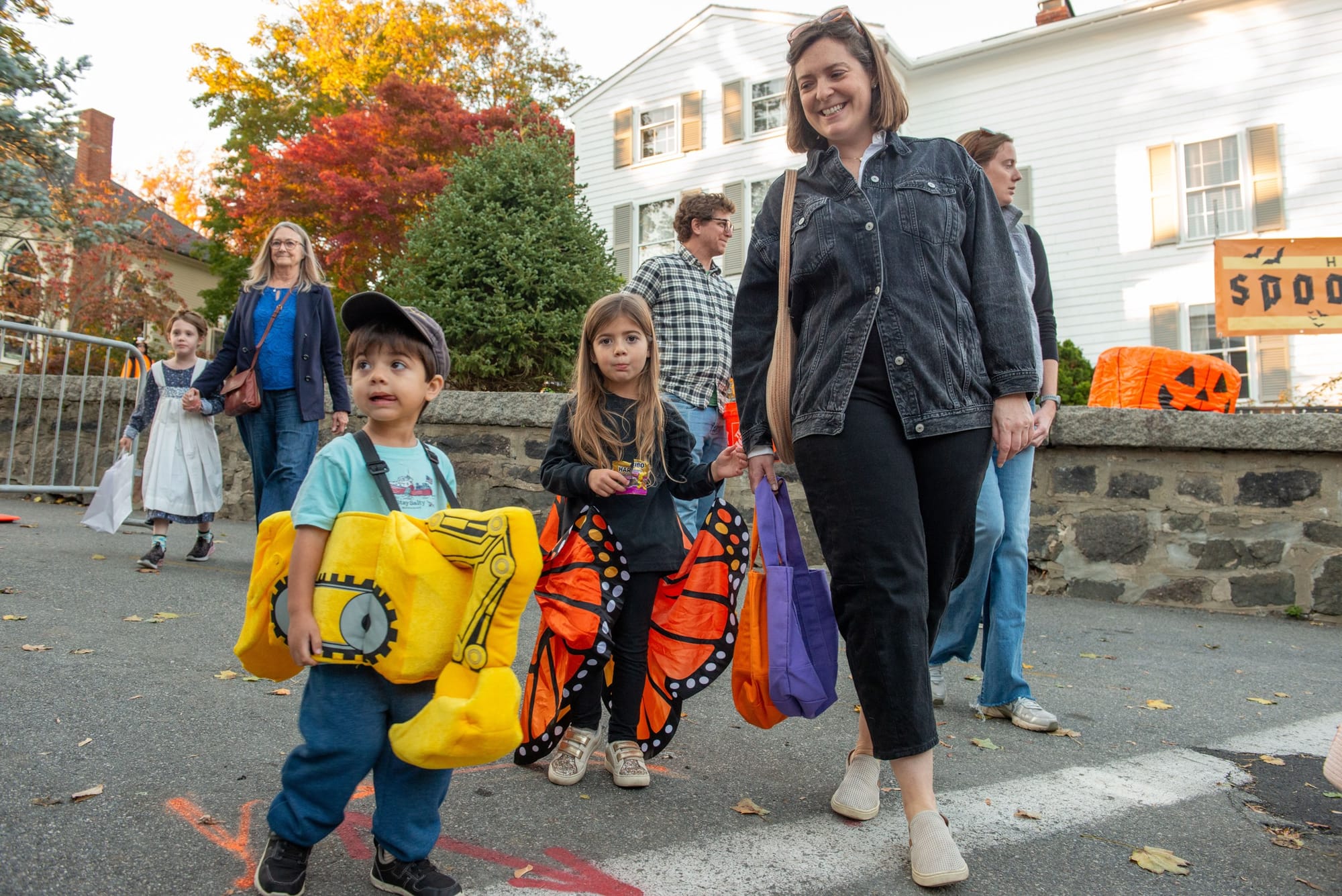 Boy in a yellow excavator costume and girl with orange butterfly wings walk with a woman