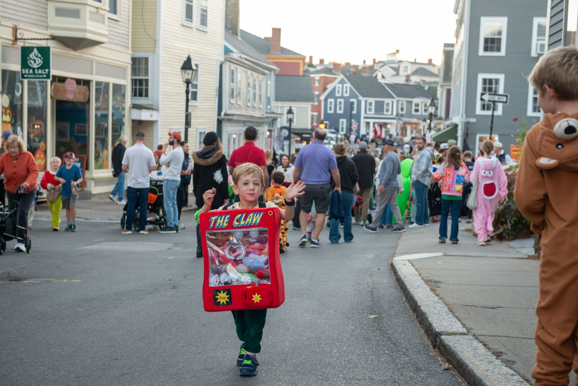 Child in a red claw machine costume waves on a busy street