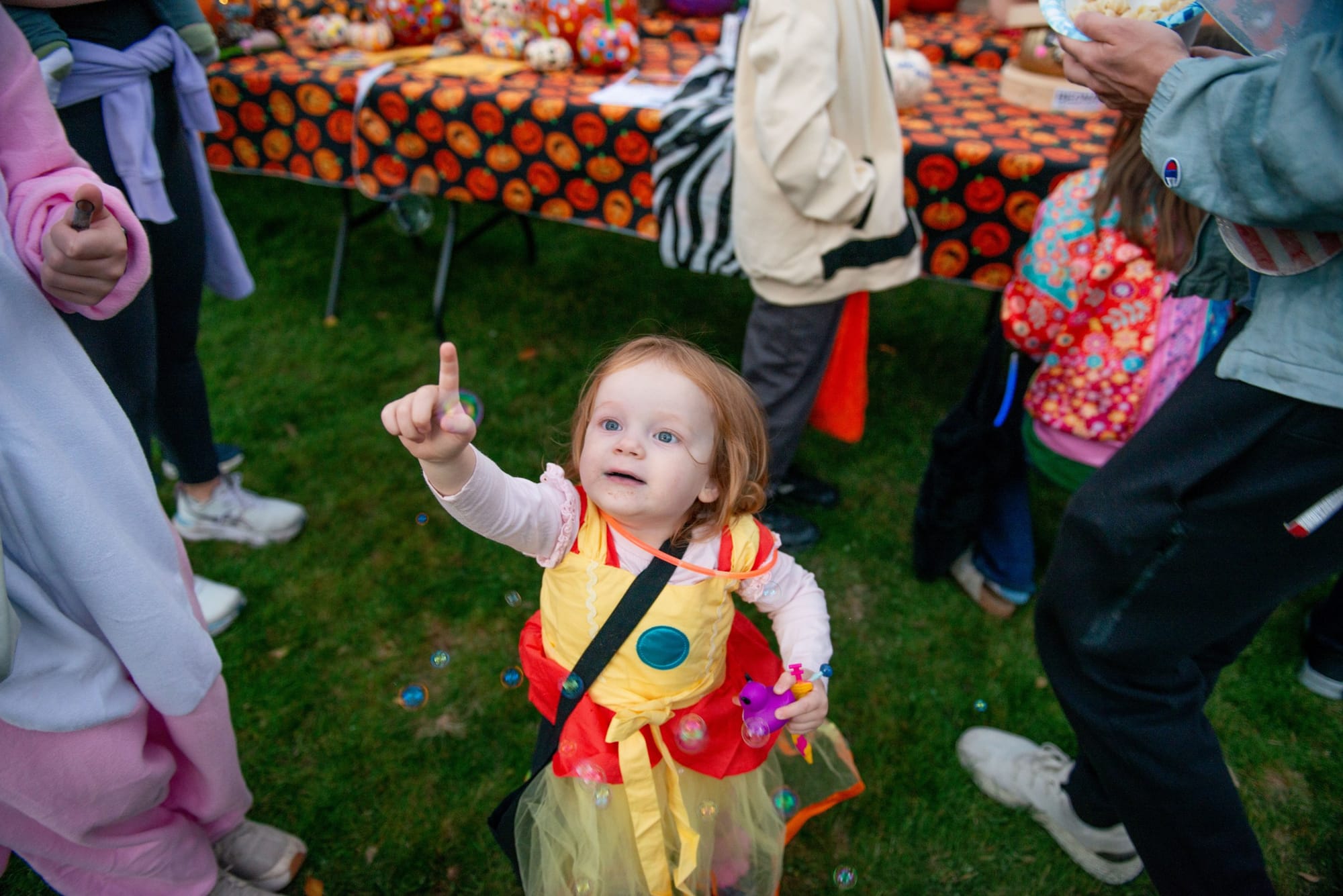 Toddler in a yellow and red costume points up at bubbles