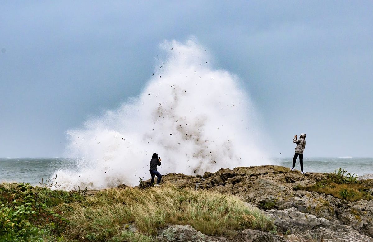 Two onlookers photograph a towering wave as it explodes over the rocks at Chandler Hovey Park