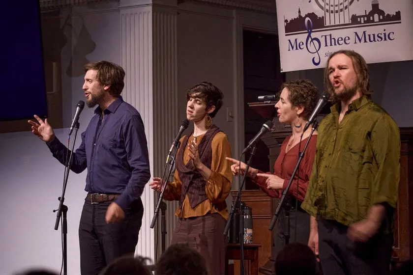 Four singers performing at microphones on stage beneath a Me & Thee Music banner