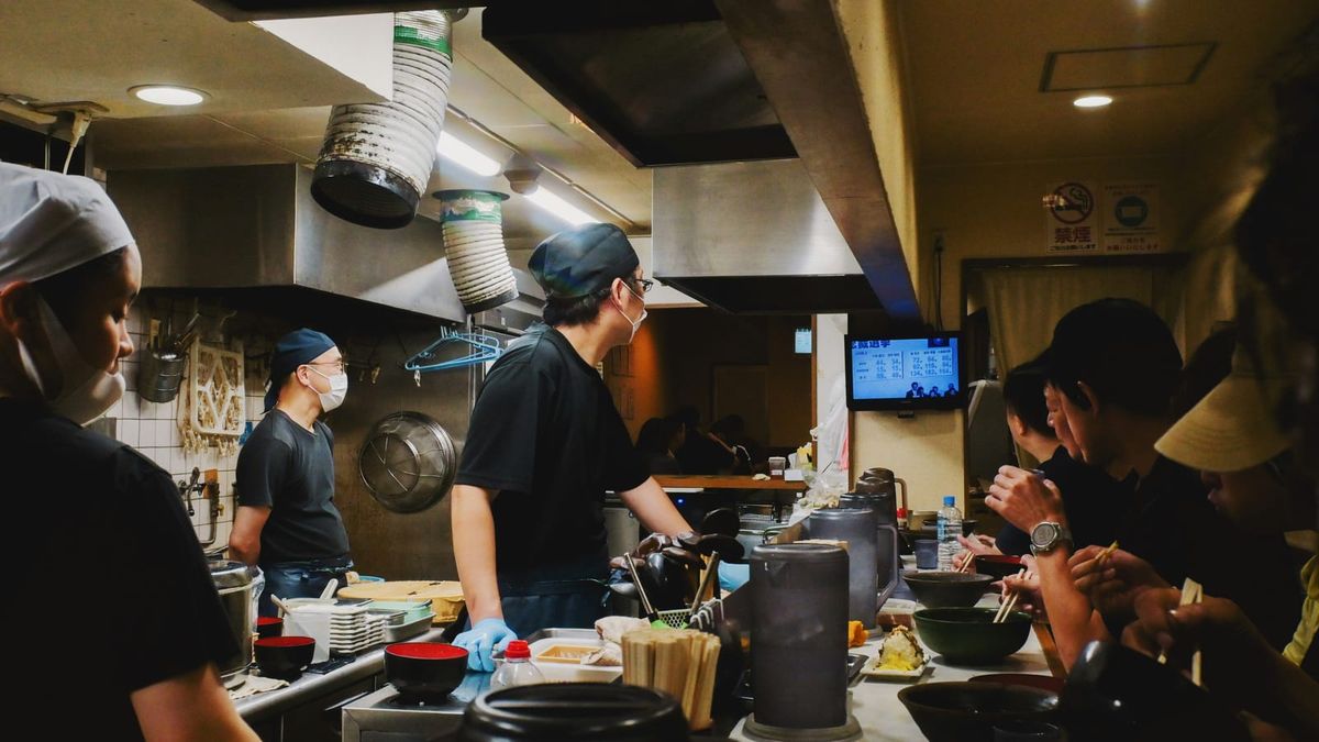 Cooks and diners on opposite sides of a restaurant service counter in Osaka.