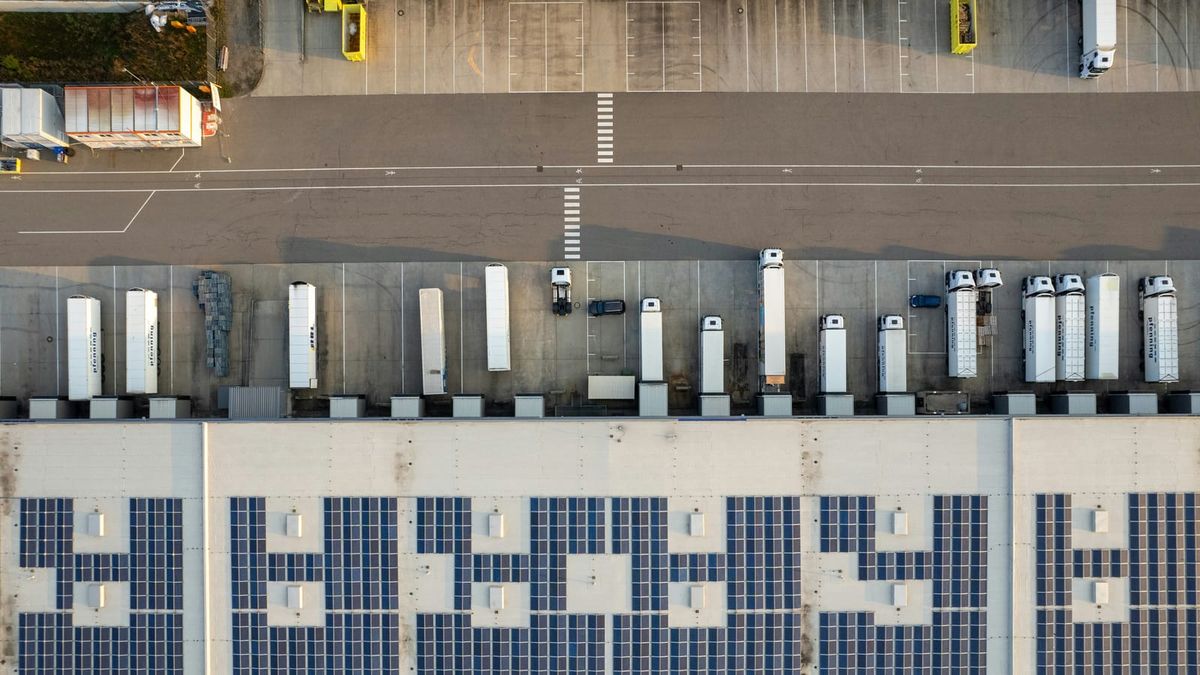 Aerial photograph of freight trucks lined up at warehouse loading docks, with long shadows across the yard.