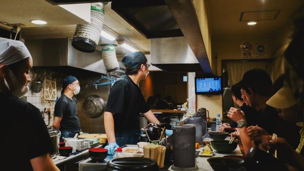 Cooks and diners on opposite sides of a restaurant service counter in Osaka.