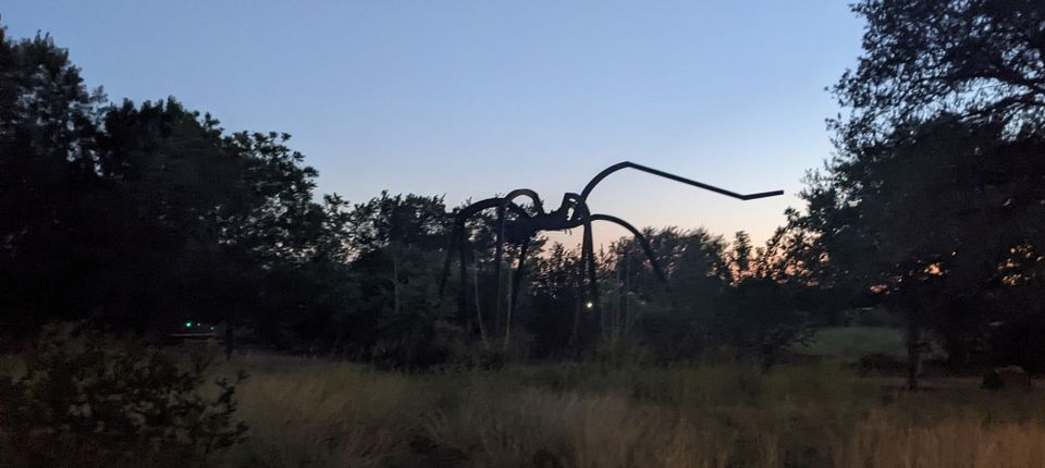 a giant spider in front of the dusky sky in austin with its front leg raised