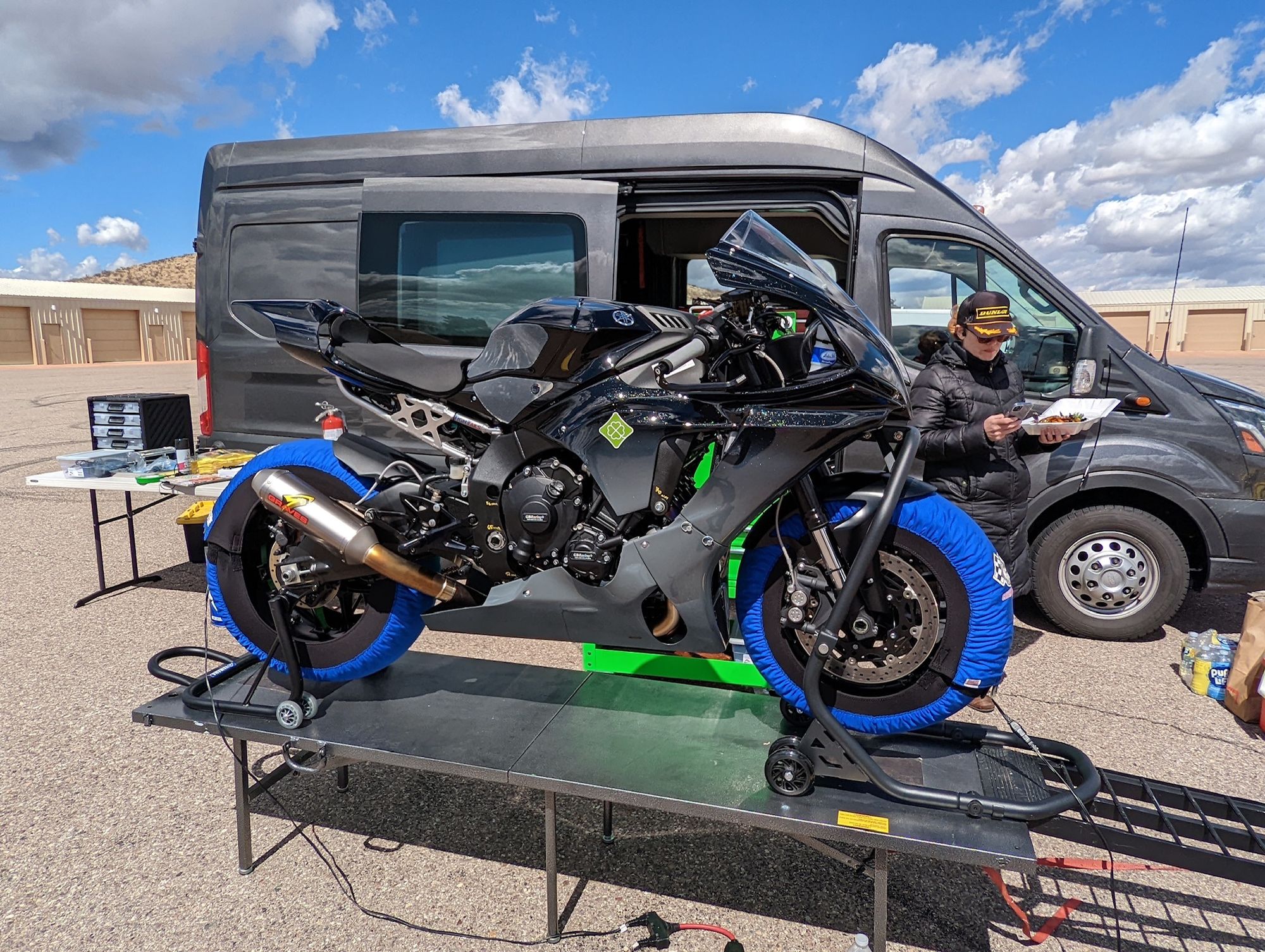 Me, balancing my lunch on one hand and press outreach on my phone on the other, walking behind this year's race bike up on a paddock stand.