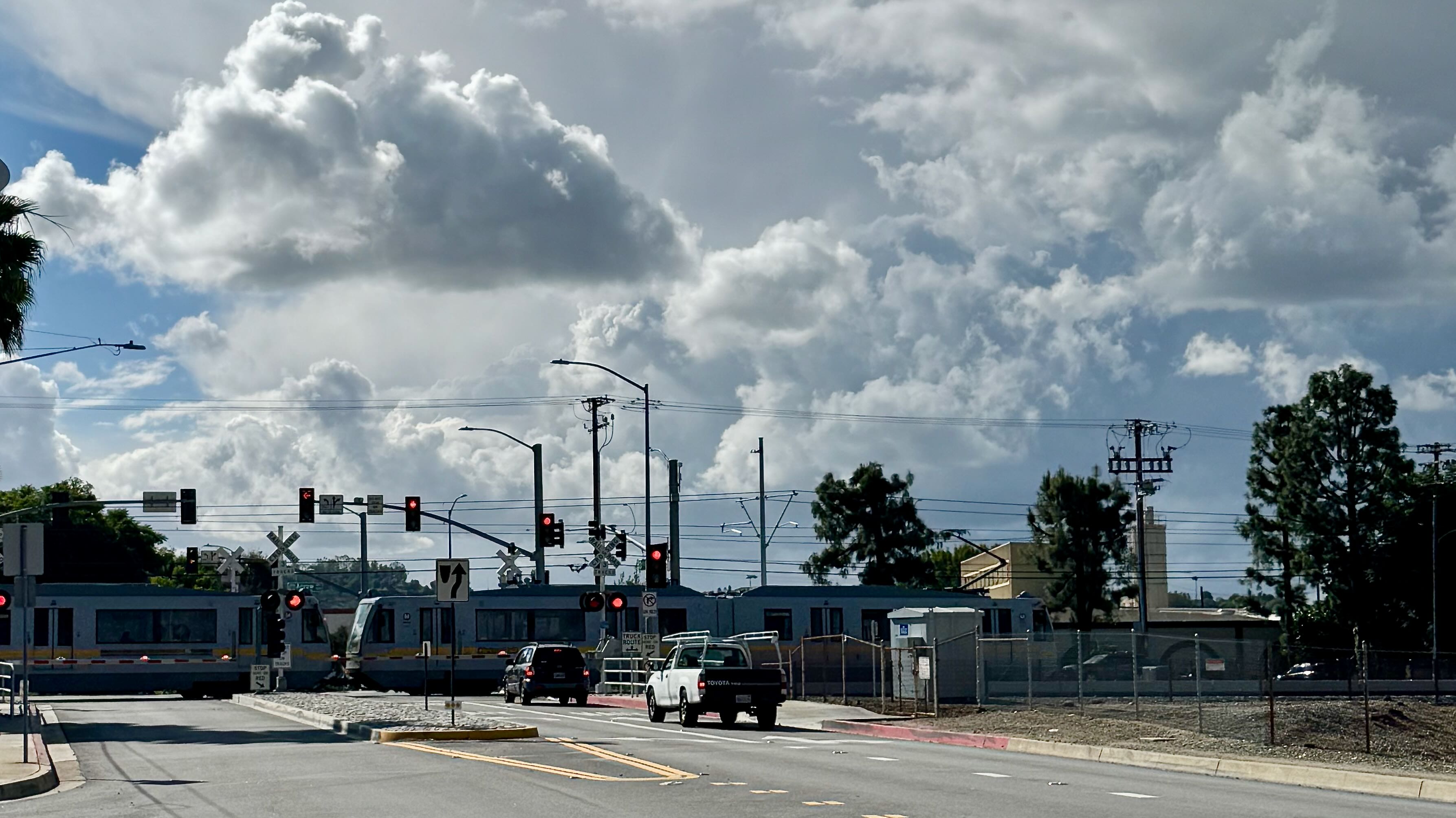 Cars stopped at a signal at the LA Metro track and a Metro train going by.
