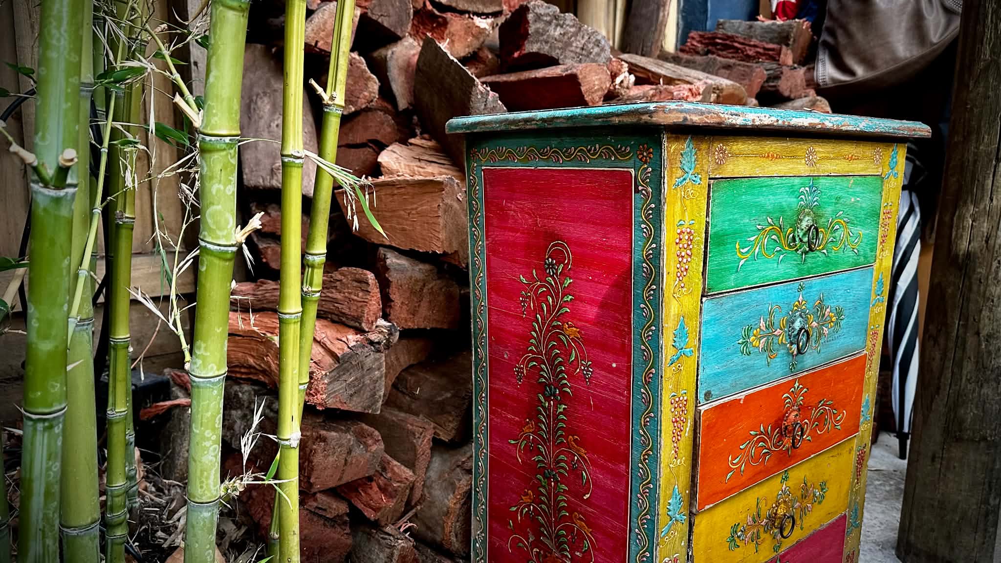 A brightly painted chest of drawers beside green bamboo and a stack of split firewood in Café Go’s garden.