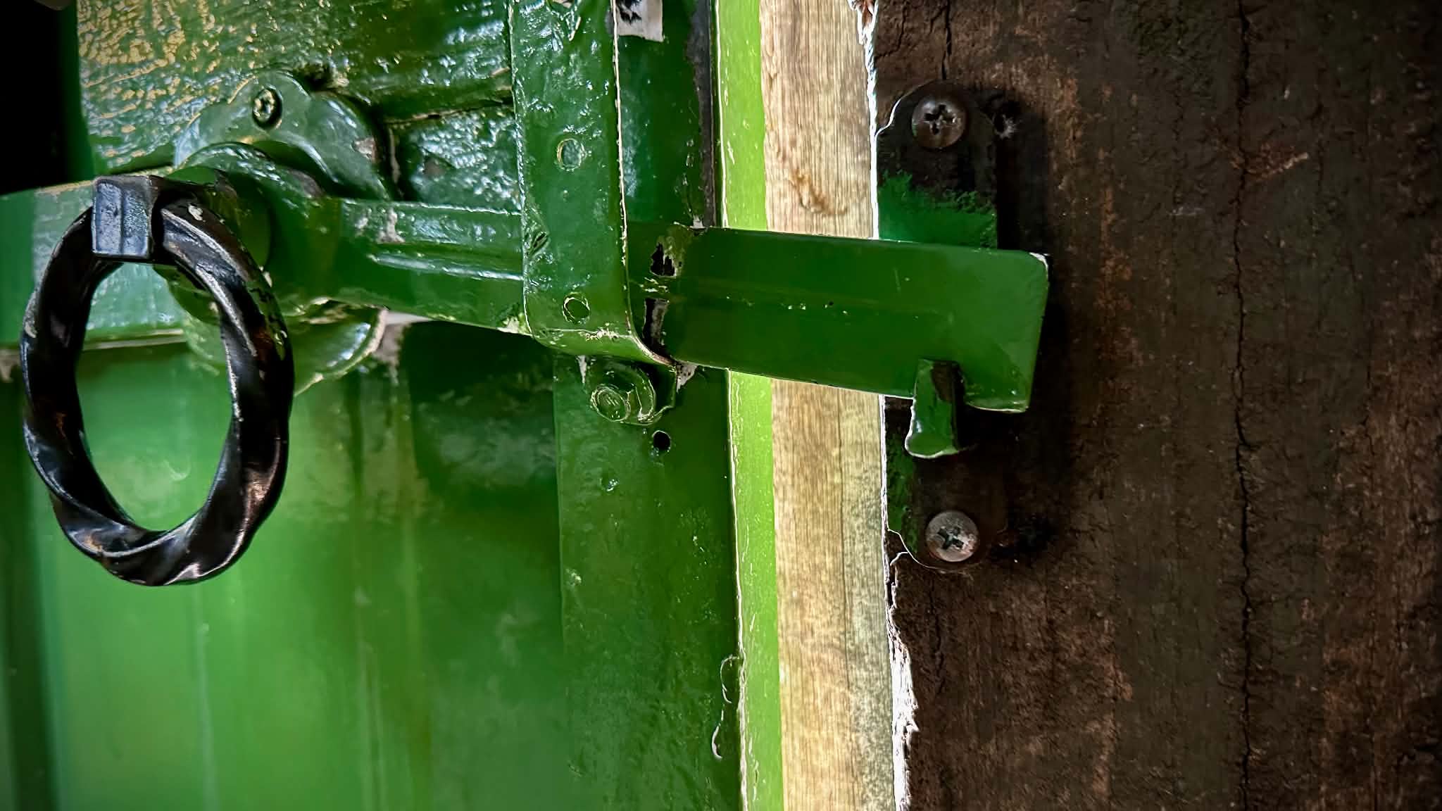 Close-up of a green-painted metal latch and black ring handle fixed to a timber gate at the rear entry to Café Go.
