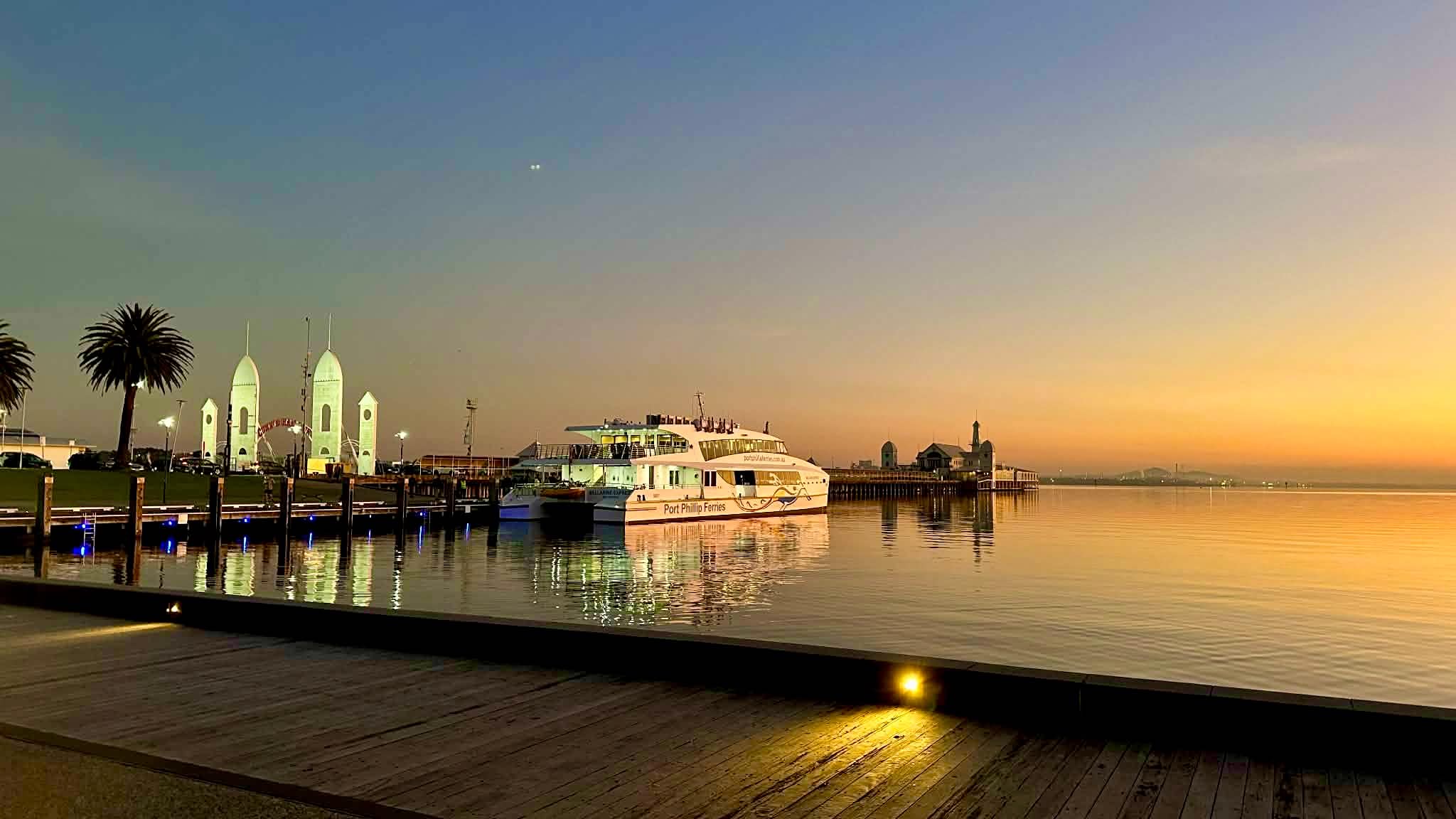 A Port Phillip Ferries catamaran on the water near Cunningham Pier, with the white pier building beyond.