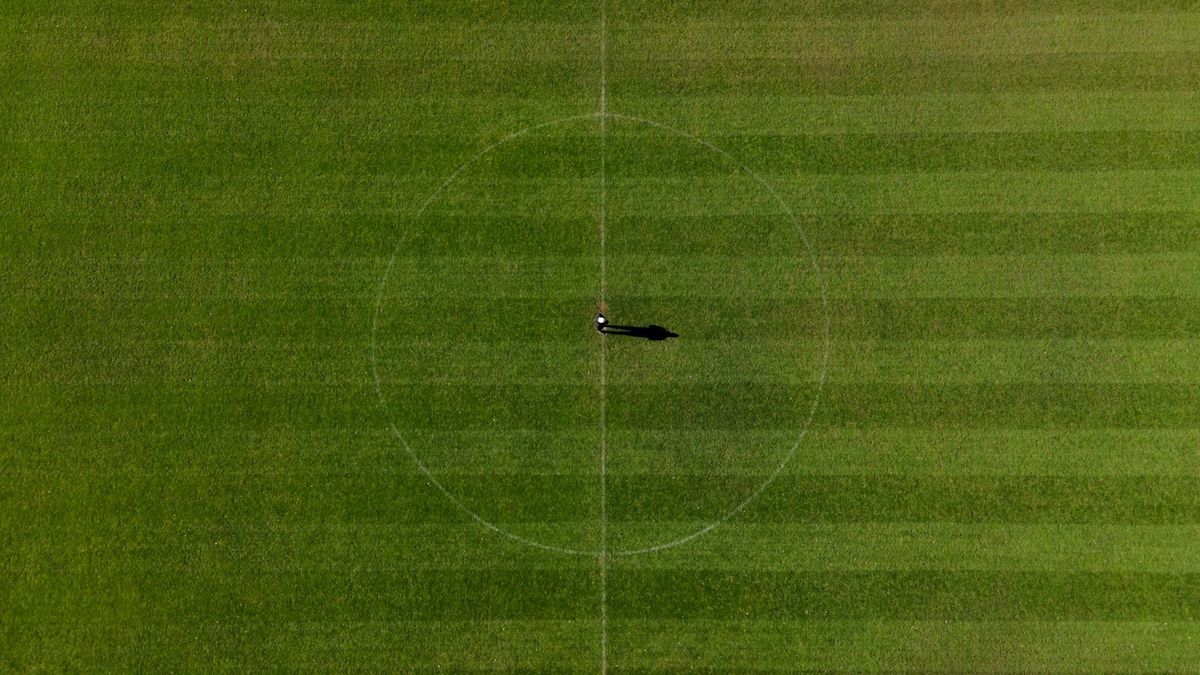 Aerial view of a grass soccer pitch with a single player standing at the center dot