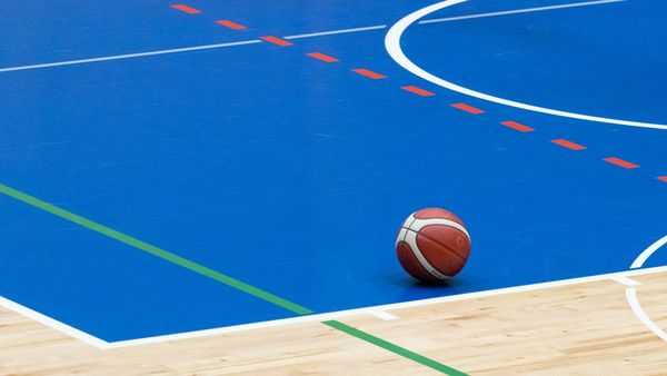 The view of a basketball court at floor level. An orange and white basketball appears in the bottom right corner of the composition.