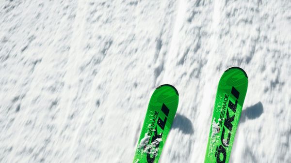 The tips of a pair of bright green skis are shown against the background of groomed white snow