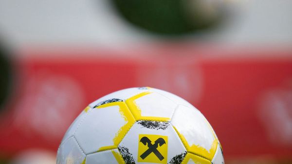 The top of a white and yellow soccer ball sits against a blurred white and red background