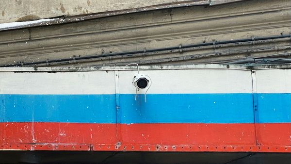 Photo of a security camera mounted to the side of an overhang that is painted with three horizontal stripes of white, blue, and red