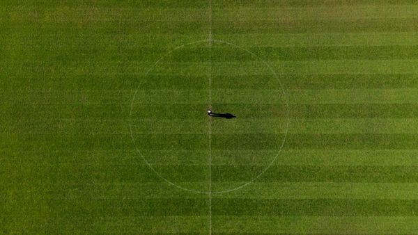 Aerial view of a grass soccer pitch with a single player standing at the center dot