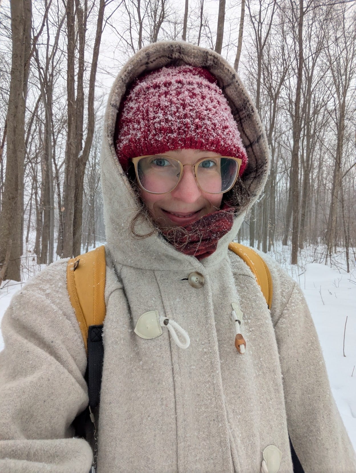 Selfie of a white person in the snowy woods, bundled up in warm clothes and smiling broadly