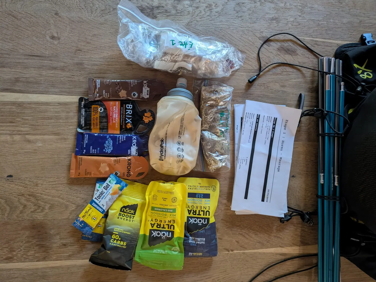 Sur une table en bois, gels et sachets d’énergie de randonnée, bâtons bleus, instructions « Étape 1 : Hornu - Maurage » visibles.