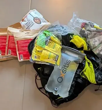 Sac de trail en itinérance sur lequel une poche d'eau est déposée, des aliments lyophilisés et sportifs