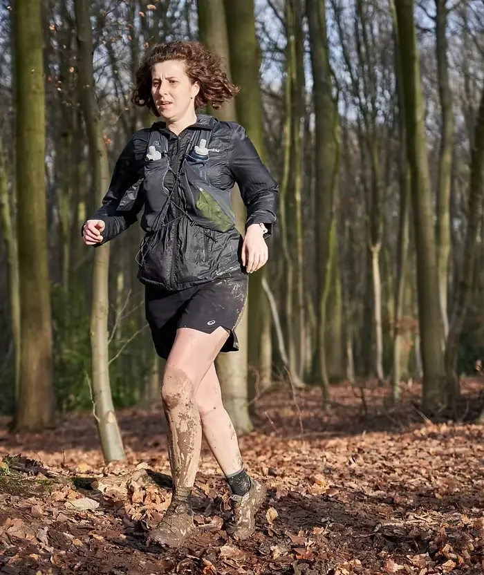 Femme habillée en noir, courant dans les bois et la boue sous le soleil