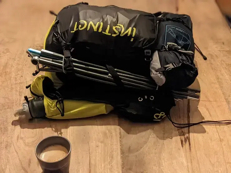 Sac de trail noir et jaune déposé sur une table de bois à côté d'une tasse de café