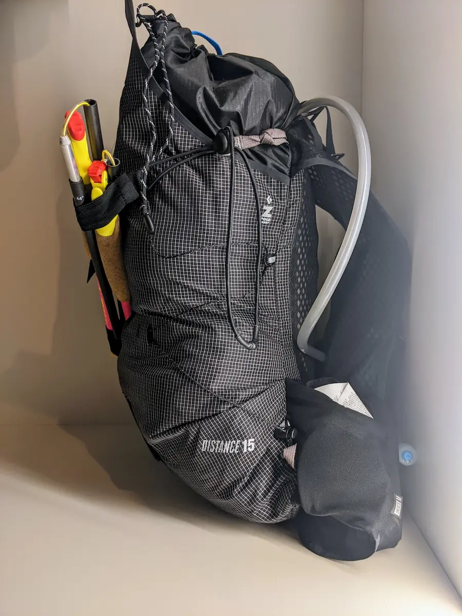sac de trail noir pour l'itinérance, tuyau d'eau et bâtons accrochés sur l'extérieur du sac