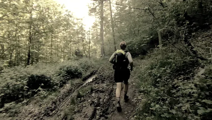 Coureuse trail en itinérance sentier boueux avec sac sur dos, environnement boisée