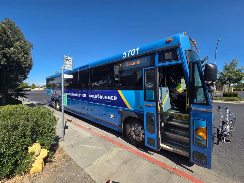 A blue Gold Runner Route 5 motorcoach stopped at the curb on Ninth Street in Orland, beside a Glenn Ride bus stop sign.