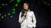 Asha Sharma holding a microphone on a backlit stage