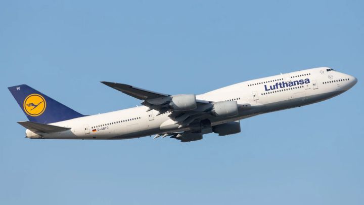A Lufthansa Boeing 747-8 airliner, registered as D-ABYQ, takes off against a clear blue sky, showing its iconic hump and the company's crane logo on the tail fin.