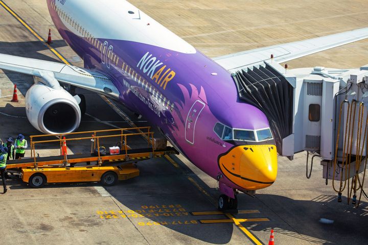 Nok air parked in the runway with the jetbridge attatched and ground staff present around it for inspection purposes.