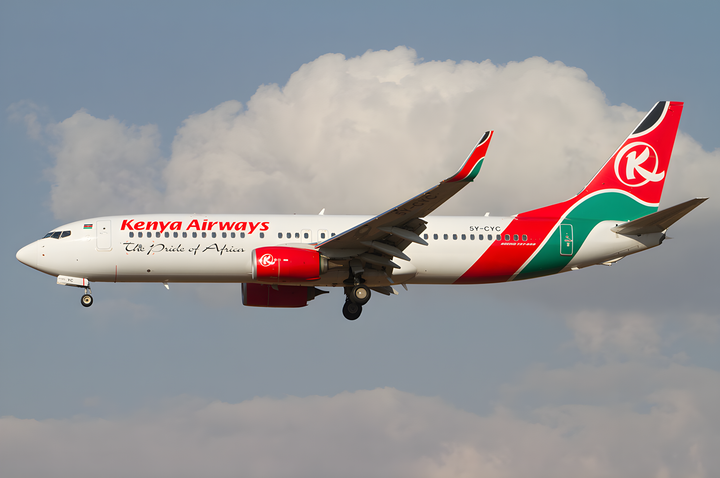 Kenya Airways Boeing 737 (5Y-CYC) in white, red, and green livery with ‘The Pride of Africa,’ flying against clouds.