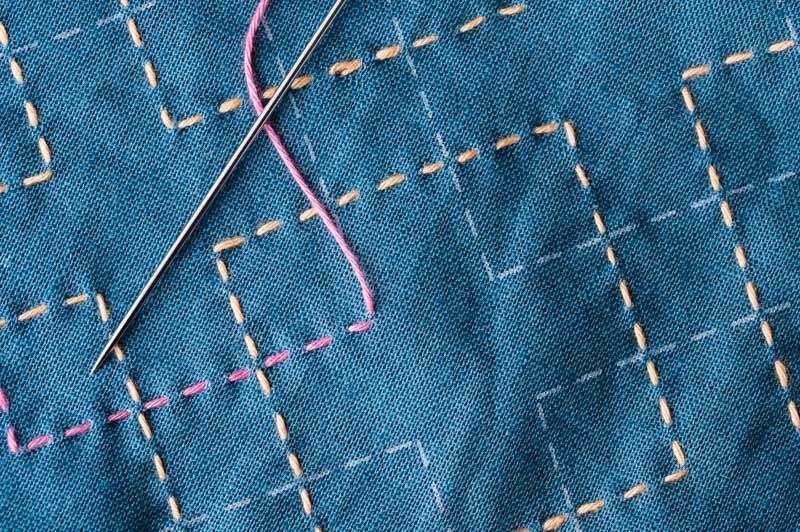 Running stitch in orange and pink on teal cloth