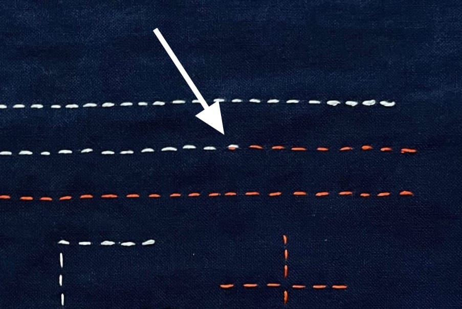 Indigo fabric with white and red stitches showing how to connect threads