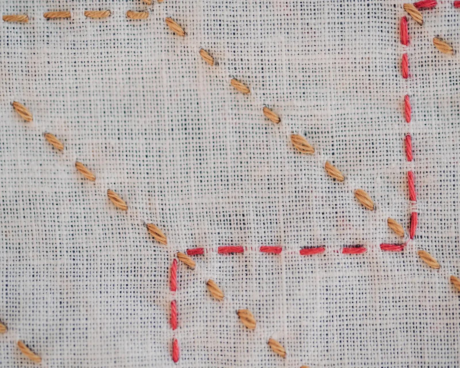 The yabane sashiko pattern in mustard and red thread on white fabric.