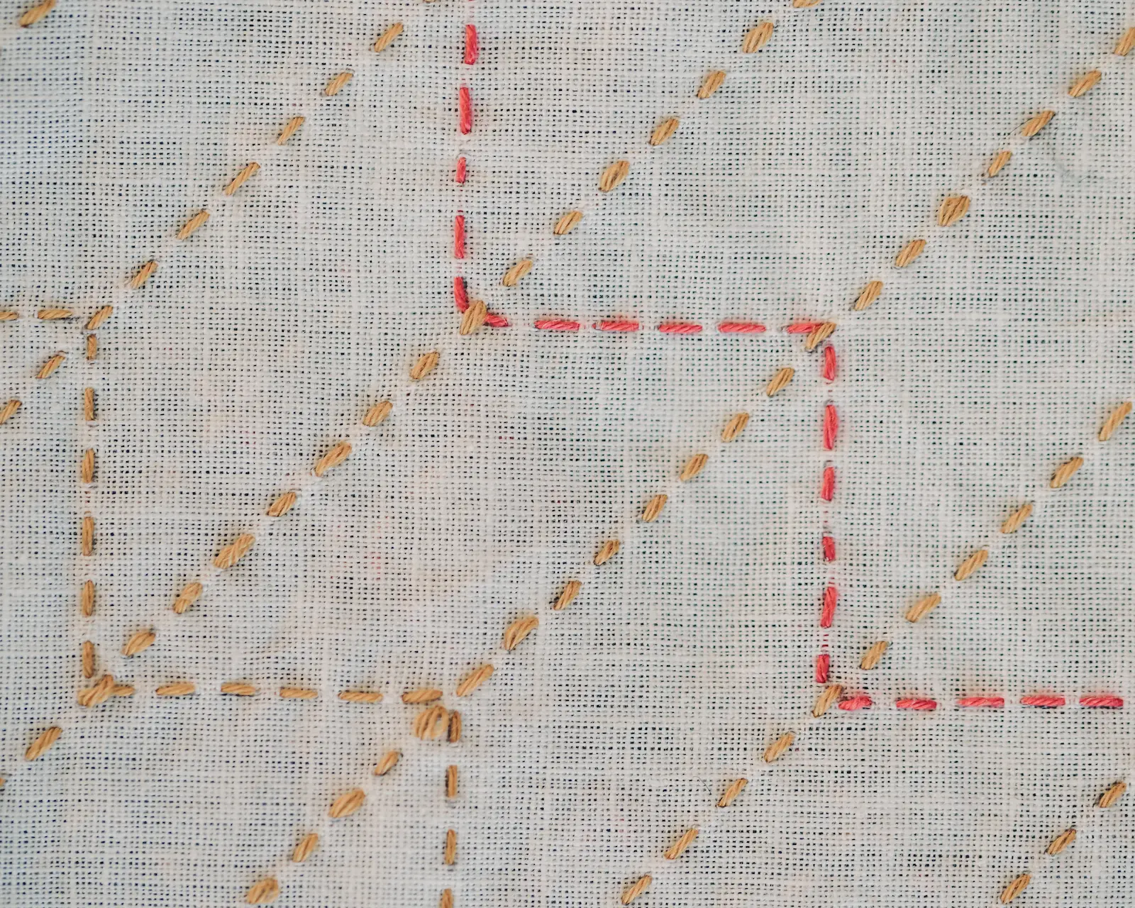 The yabane sashiko pattern in mustard and red thread on white fabric.