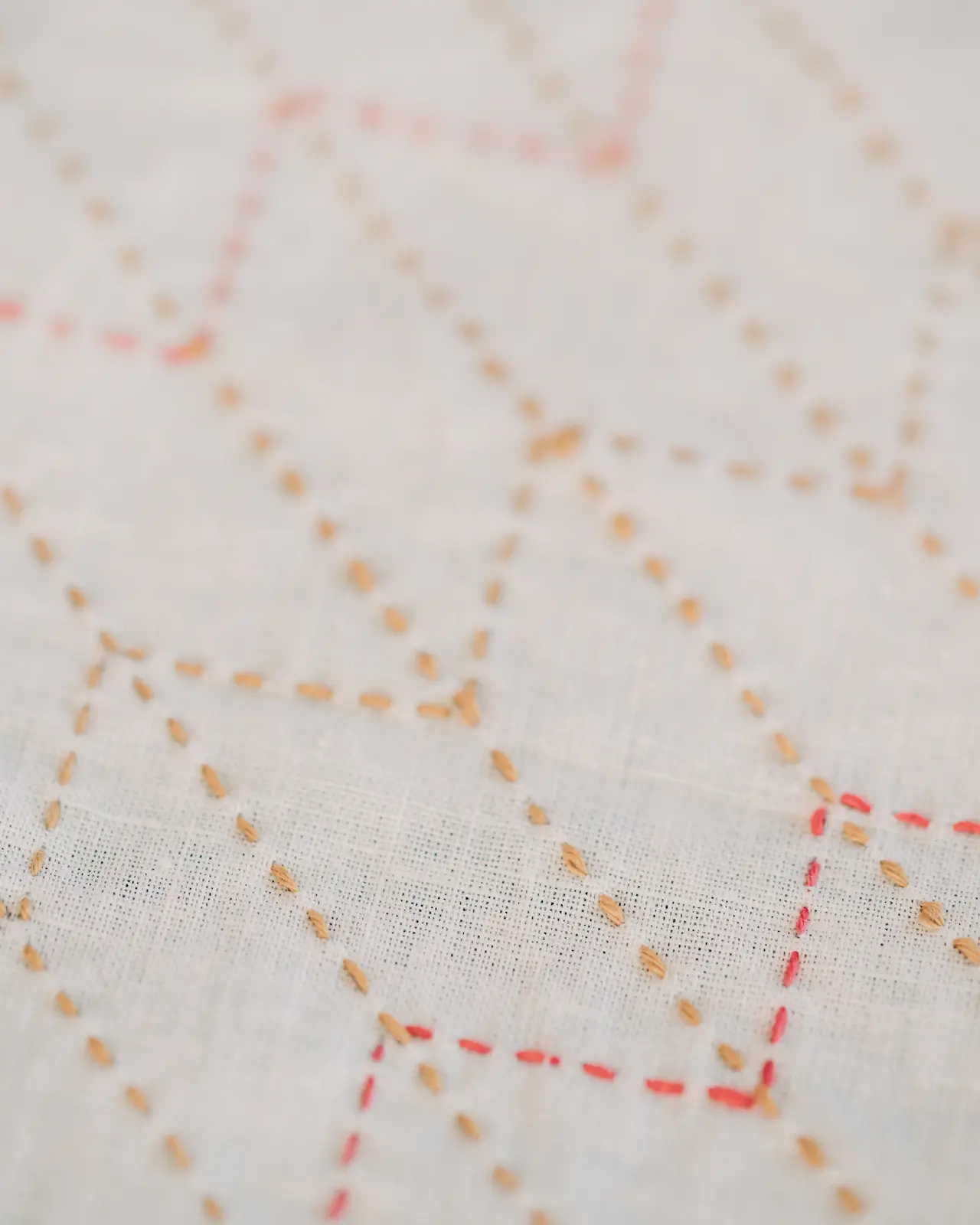 The yabane sashiko pattern in mustard and red thread on white fabric.