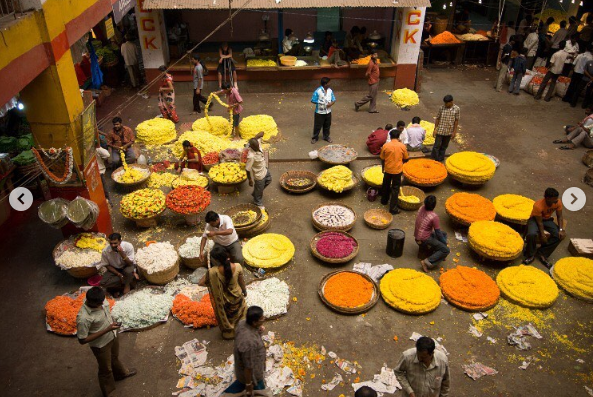 Flower market or phool market with red, yellow and orange flowers. The vendors are standing or sitting next to the flowers which are in cane baskets.